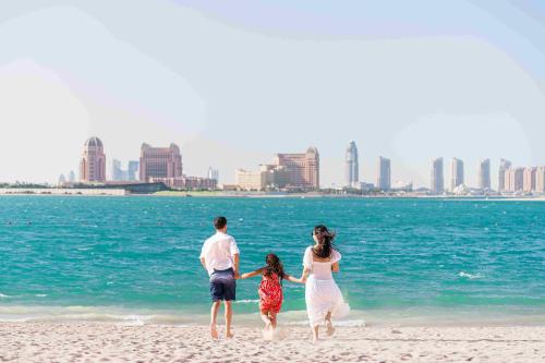 a family walking on the beach near the water at Kingsgate Hotel Doha by Millennium Hotels in Doha