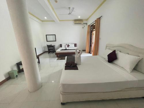 a white bedroom with a large bed and a table at Hotel Sobana Lake front in Udawalawe