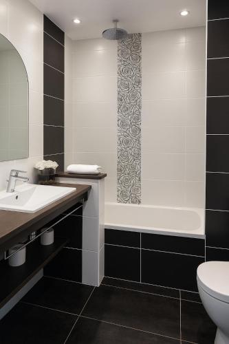 a bathroom with a sink and a tub and a toilet at Hotel & Spa Gil de France Cap d'Agde in Cap d'Agde