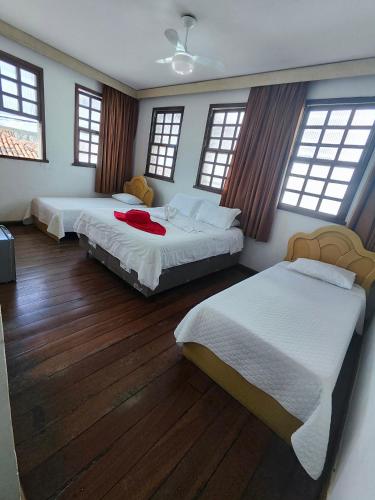 two beds in a room with wooden floors and windows at Pousada Flor de Lis in Diamantina