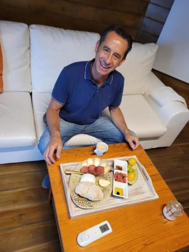 a man sitting on a couch with a table with a plate of food at The Vie Llage - Authorial Suites Bungalows in Vagos