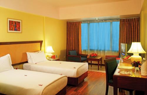 a hotel room with two beds and a desk at Classic Sarovar Portico Trivandrum in Trivandrum