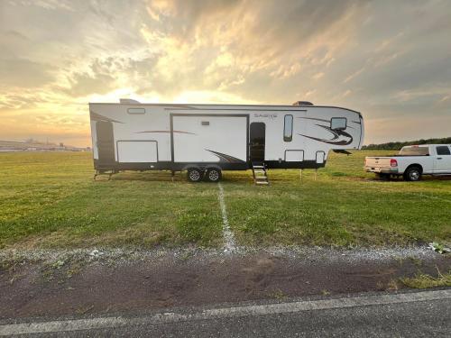 a white trailer parked in a field with a truck at Luxury Lakeside Retreat - The Cozy Wondrous Weekendator in Lake Ariel
