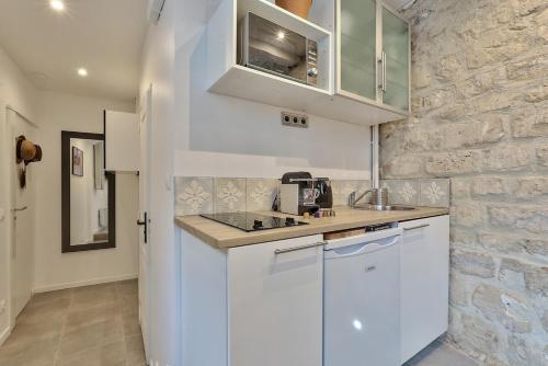 - une cuisine avec des placards blancs et un mur en pierre dans l'établissement Studio walking distance from Marais with mobile AC, à Paris