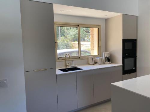 une cuisine blanche avec un évier et une fenêtre dans l'établissement Charming stone villa with pool, à Figari