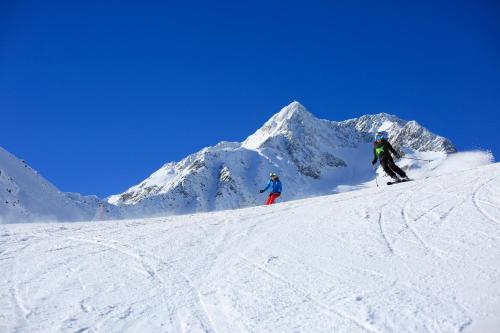 two people are skiing down a snow covered mountain at Hotel Vernagt in Senales