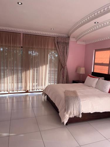 a bedroom with a large bed with pink walls and large windows at The Serene Gift in Mbabane