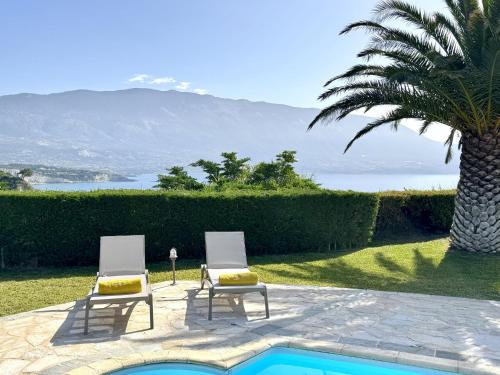 two chairs sitting next to a swimming pool with a palm tree at Villa Hephaestus Spartia Kefalonia in Spartia