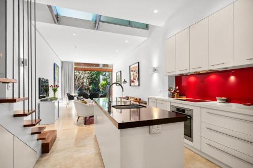 a kitchen with white cabinets and a red accent wall at Stylish Fully Renovated Luxe 3BR, 2BA Balmain Terrace near Parks, Ferry, Cafes & Pubs in Sydney