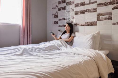 a woman laying in bed looking at her cell phone at Hotel Moon Cheonan ShinBuldang in Cheonan