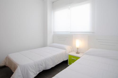 two beds in a white room with a window at Residencial Linnea Sol by Mar Holidays in Playas de Orihuela