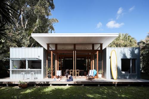 Una casa con gente sentada en una terraza con una tabla de surf. en Blueys Shack, en Blueys Beach