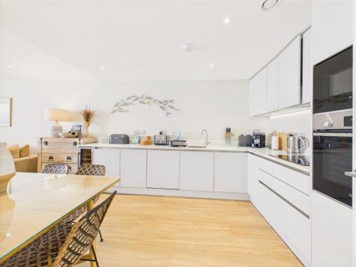 a kitchen with white cabinets and a dining table at Luxury 3-bed apartment, with direct beach access, free parking & sea views ! in Falmouth