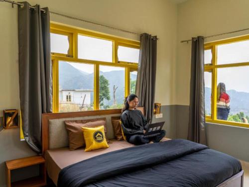 a woman sitting on a bed using a laptop at The Hosteller Kareri in Dharamshala