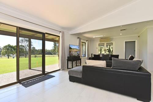 a living room with a black couch and a piano at Blaxlands Kangaroo Homestead with Hot Tub walk to Concerts and Wineries in Pokolbin
