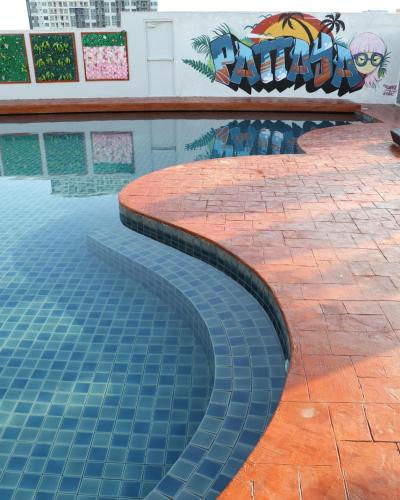 a swimming pool with blue tiles in front of a wall at Journeyhub Pattaya Central in Pattaya