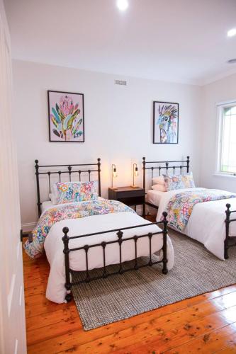 two beds in a bedroom with white walls and wood floors at Escape to a timeless getaway in Provincial Vic in Ballarat