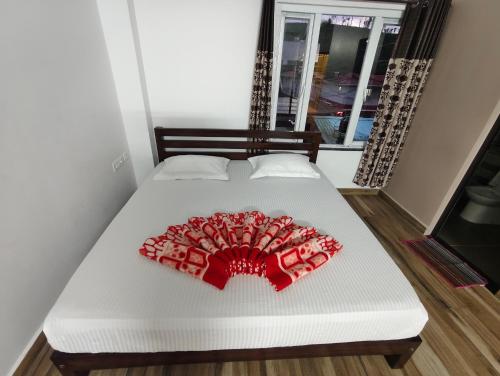 a white bed with a red decoration on it at Hornbill Castle in Vālpārai