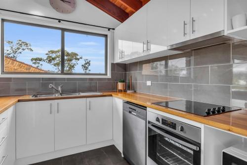 a kitchen with white cabinets and a window at Retreat on Reid Street in Merimbula