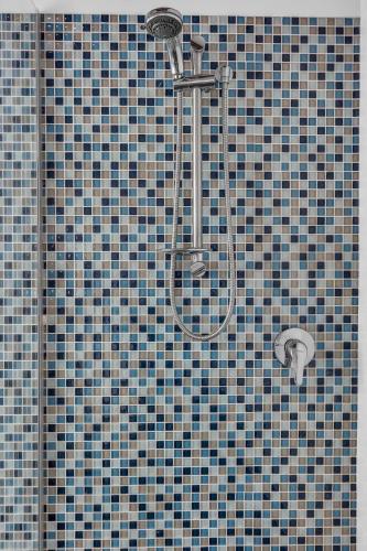 a shower in a bathroom with blue and gray tiles at Retreat on Reid Street in Merimbula