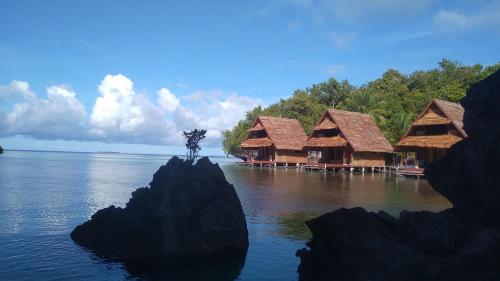 a rock in the water with a group of huts at Beser Bay Homestay in Besir