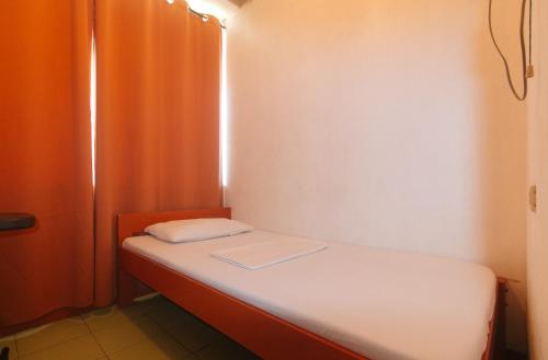 a small bed in a room with an orange curtain at Stay Malate Hostel by RedDoorz in Manila