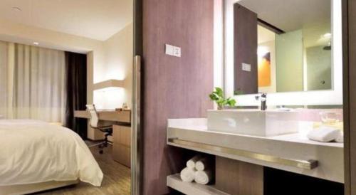 a bathroom with a sink and a bed and a mirror at Jinjiang Metropolo Shanghai Xujiahui Nanhuating Hotel in Shanghai