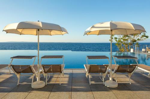 a group of chairs and umbrellas next to a pool at Vitality Hotel Punta in Veli Lošinj