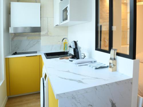 une cuisine avec des comptoirs en marbre blanc et des armoires jaunes dans l'établissement Le Petit Jacques Cognac Studio, à Cognac