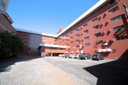 a large red building with cars parked in a parking lot at Copas Executive Hotel in Cascavel