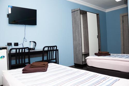 a room with two beds and a desk with a television at Hotel Tahar in Almaty