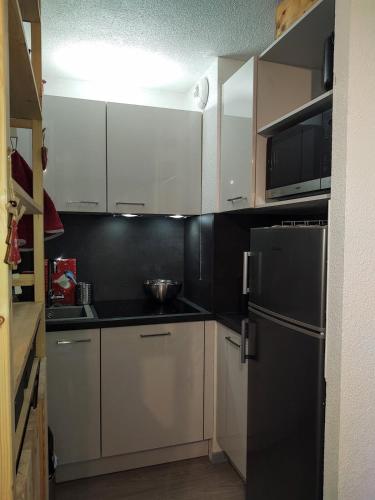une cuisine avec des armoires blanches et un réfrigérateur noir dans l'établissement Appartement au pied de la montagne, à Allos