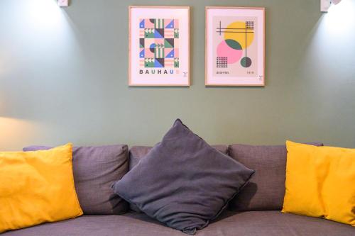 Un sofá con tres almohadas y dos cuadros en la pared. en Koukaki Beat, en Atenas