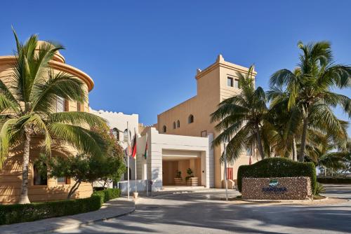 a building with palm trees in front of a street at Juweira Boutique Hotel Adult only in Salalah