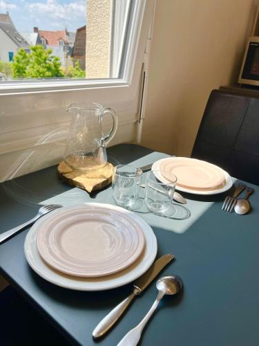 einen Tisch mit Tellern und Gläsern auf einem Tisch mit Fenster in der Unterkunft L'Hélios - T1 Bis - Bord de Sarthe in Le Mans