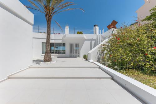 a white house with a palm tree and a sidewalk at Hastinapura, acceso directo al mar in Es Castell