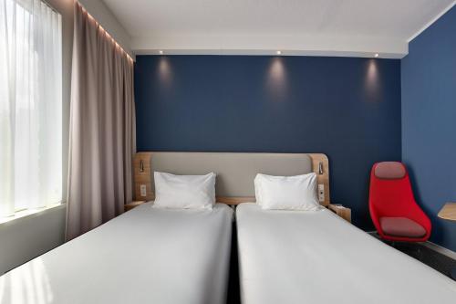 two beds in a room with a red chair at Holiday Inn Express Hasselt by IHG in Hasselt
