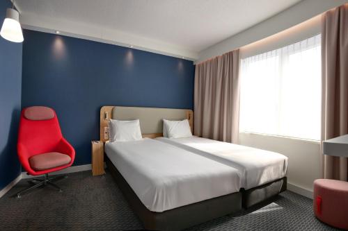 a bedroom with a bed and a red chair at Holiday Inn Express Hasselt by IHG in Hasselt