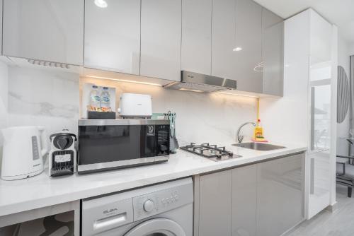 a white kitchen with a microwave and a sink at Chic and comfortable Studio Near Downtown and Canal in Dubai