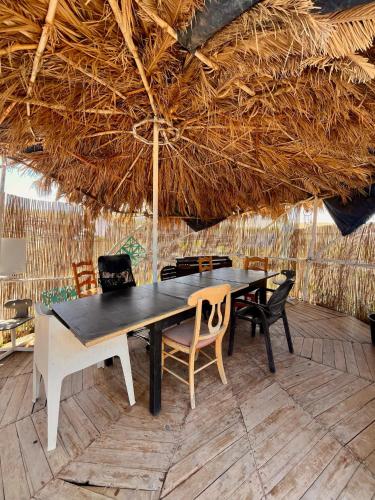 a dining table and chairs under a straw umbrella at Adeje - TwinFin Hostel & Surf Yoga Camp in Callao Salvaje