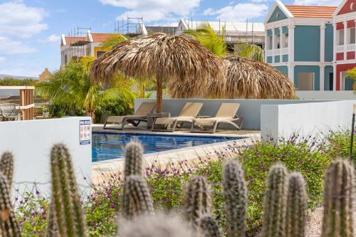 a pool with chairs and a straw umbrella and cactus at Casa Enjoy on the water of the Laguna Marina in Kralendijk