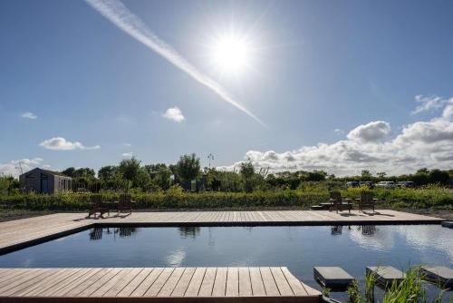 a swimming pool with benches and the sun in the sky at De Kleine Schuur at Buitenplaats Zeeuwse Liefde in Westkapelle