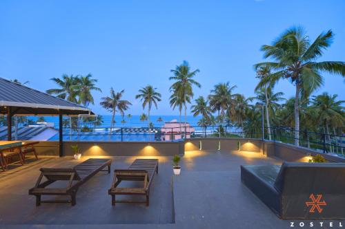 a patio with benches and tables and palm trees at Zostel Varkala in Varkala