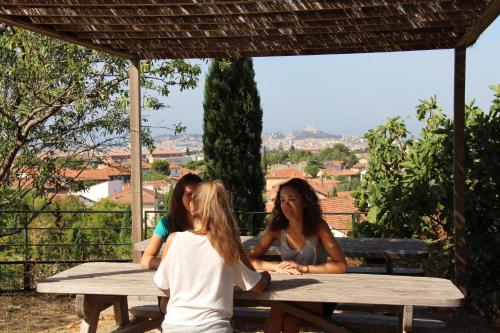 trois femmes assises à une table de pique-nique en bois dans l'établissement Auberge de Jeunesse HI Marseille Bois-Luzy, à Marseille