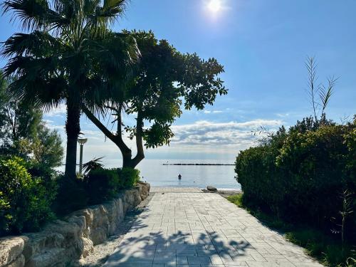 a stone walkway next to the water with palm trees at "99 steps to the beach" Beachfront apartment with Kids Room, Pool & 2 Workspaces in Limassol