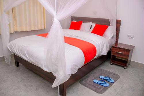 a bedroom with a large bed with red pillows and blue slippers at Goshen Paradise Hotel in Kendu Bay
