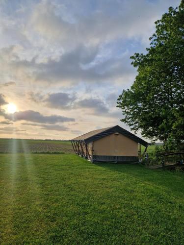 a building in a field with a tree and the sunset at Glamping Safaritent 4 persoons in Hindeloopen