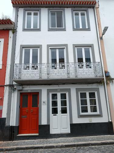 a white house with red doors and a balcony at Casa ao centro - Apartamento Angrego in Angra do Heroísmo