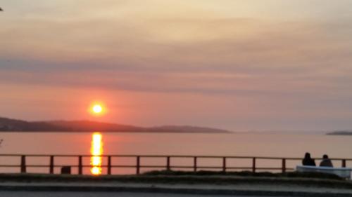 people standing on a pier watching the sunset at Hostal Vista al Mar hct in Ancud