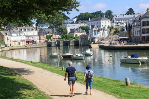 two people walking down a path near a river with boats at Maison de charme in Pluneret